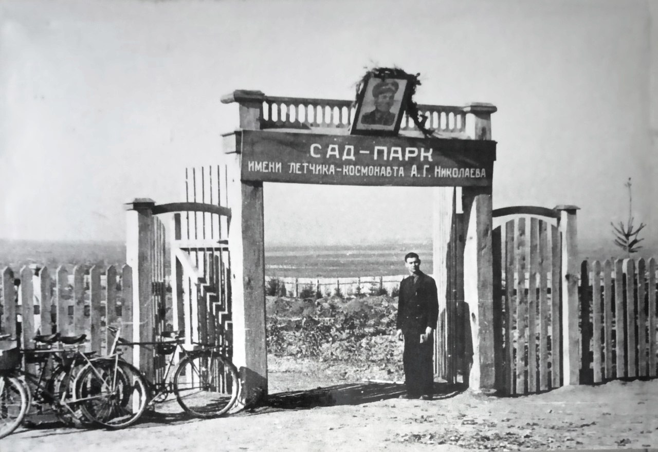 На изображении мужчина стоит перед воротами с велосипедом. Ворота изготовлены из металла и имеют...