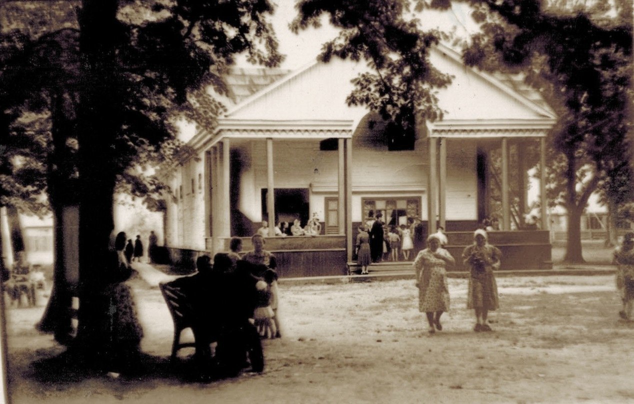 Возле здания собралась группа людей, рядом с ними стоит величественный конь. Здание выглядит...